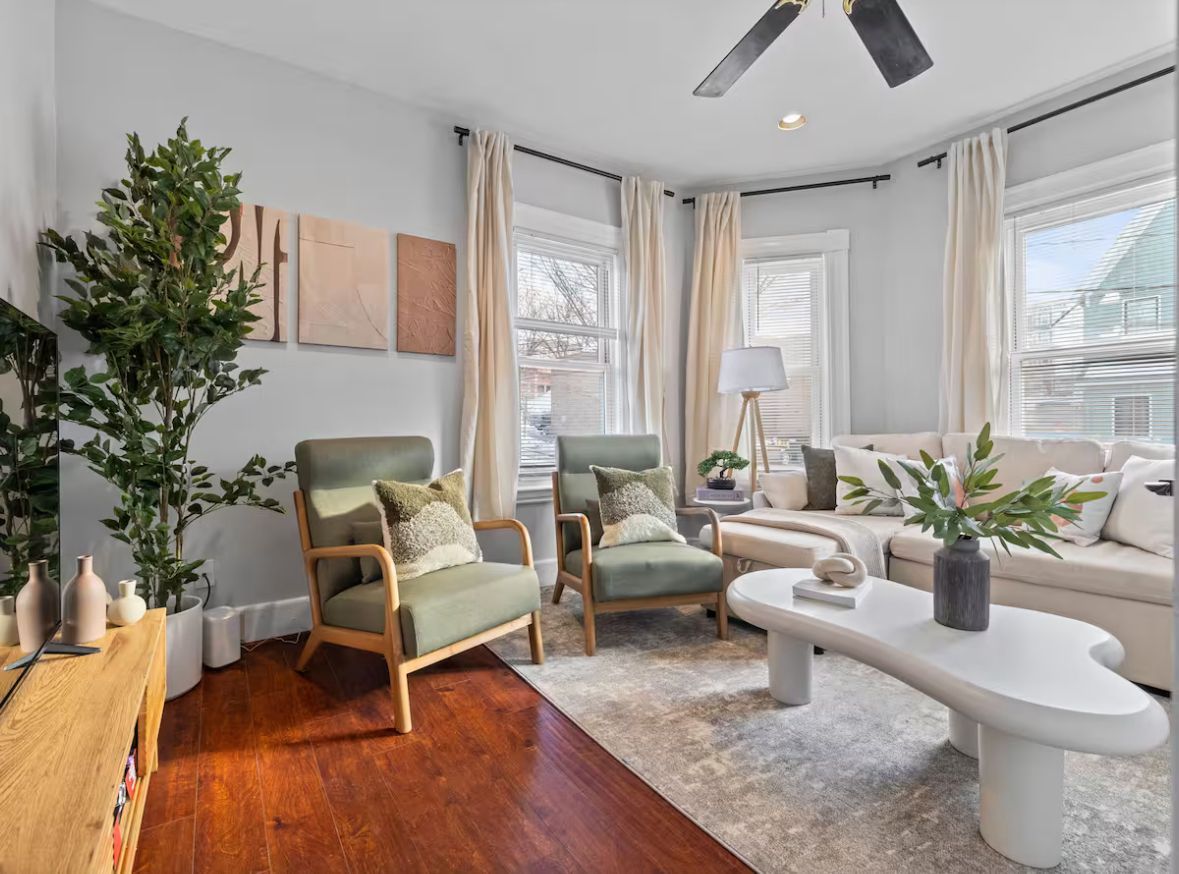 Living room with green armchairs, white couch, light rug, and bay windows.