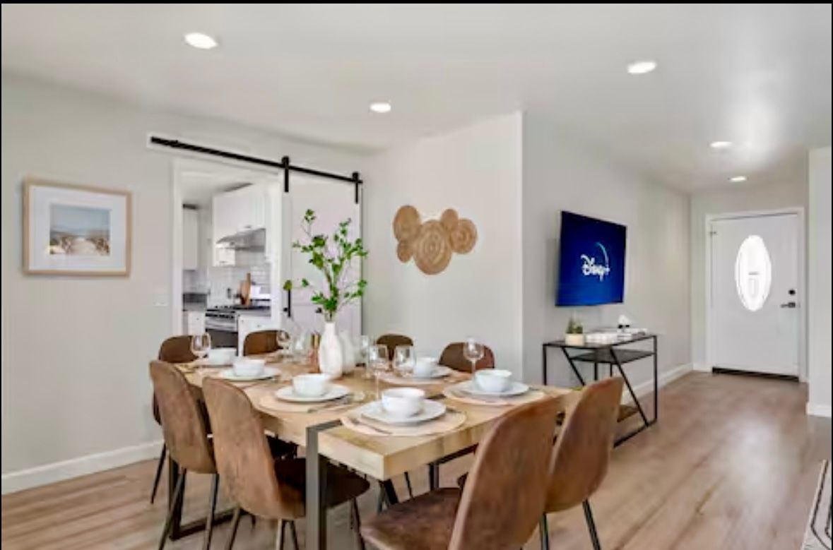 Dining room with a wooden table, chairs, and television. A barn door leads to the kitchen.