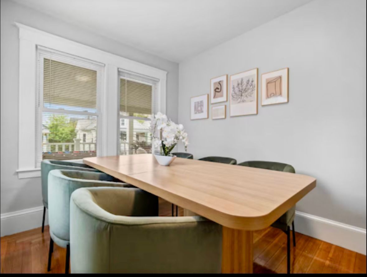 Dining room with a wooden table, blue chairs, and framed artwork on a light gray wall.