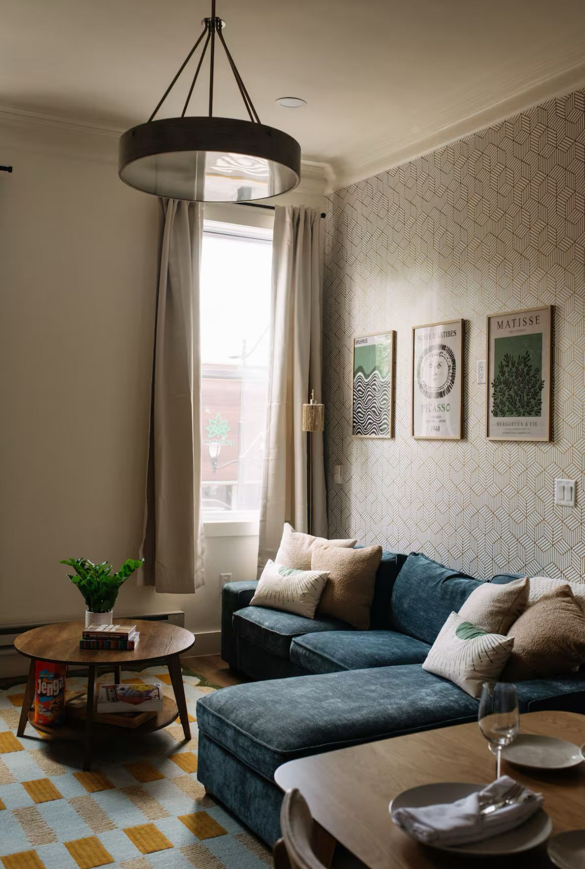 Living room with blue sectional sofa, patterned wallpaper, round wooden coffee table, and botanical prints.