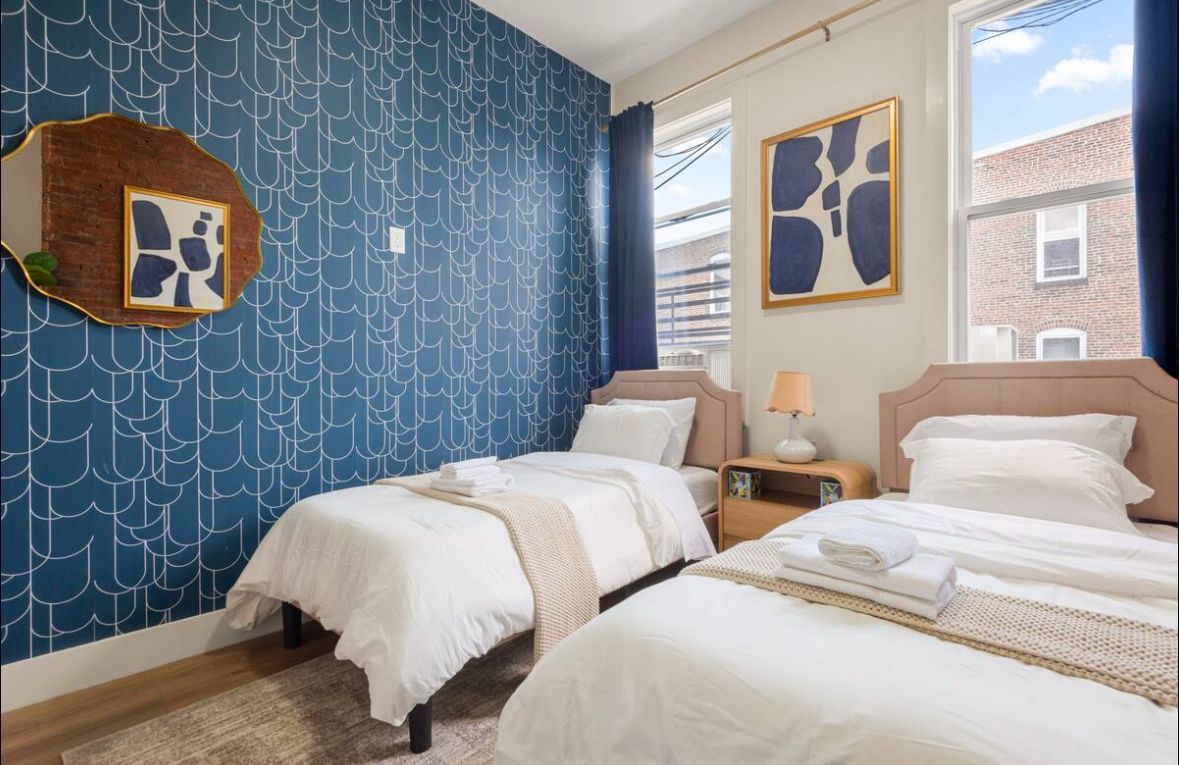 Two twin beds in a room with blue patterned wallpaper and a gold-framed mirror.