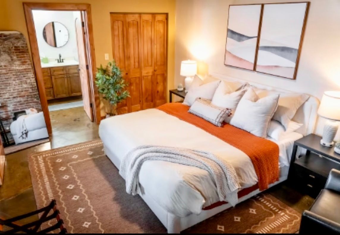 Bedroom with bed, art, rug, and open door to bathroom. Orange and white bedding.