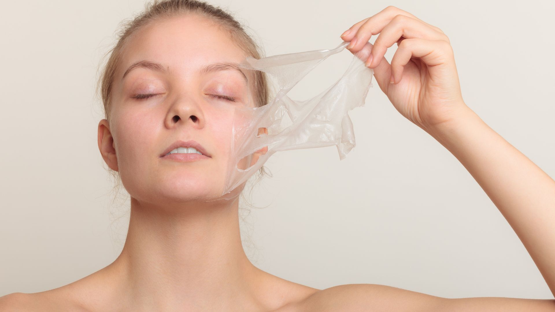 A woman is peeling off a sheet of plastic from her face.