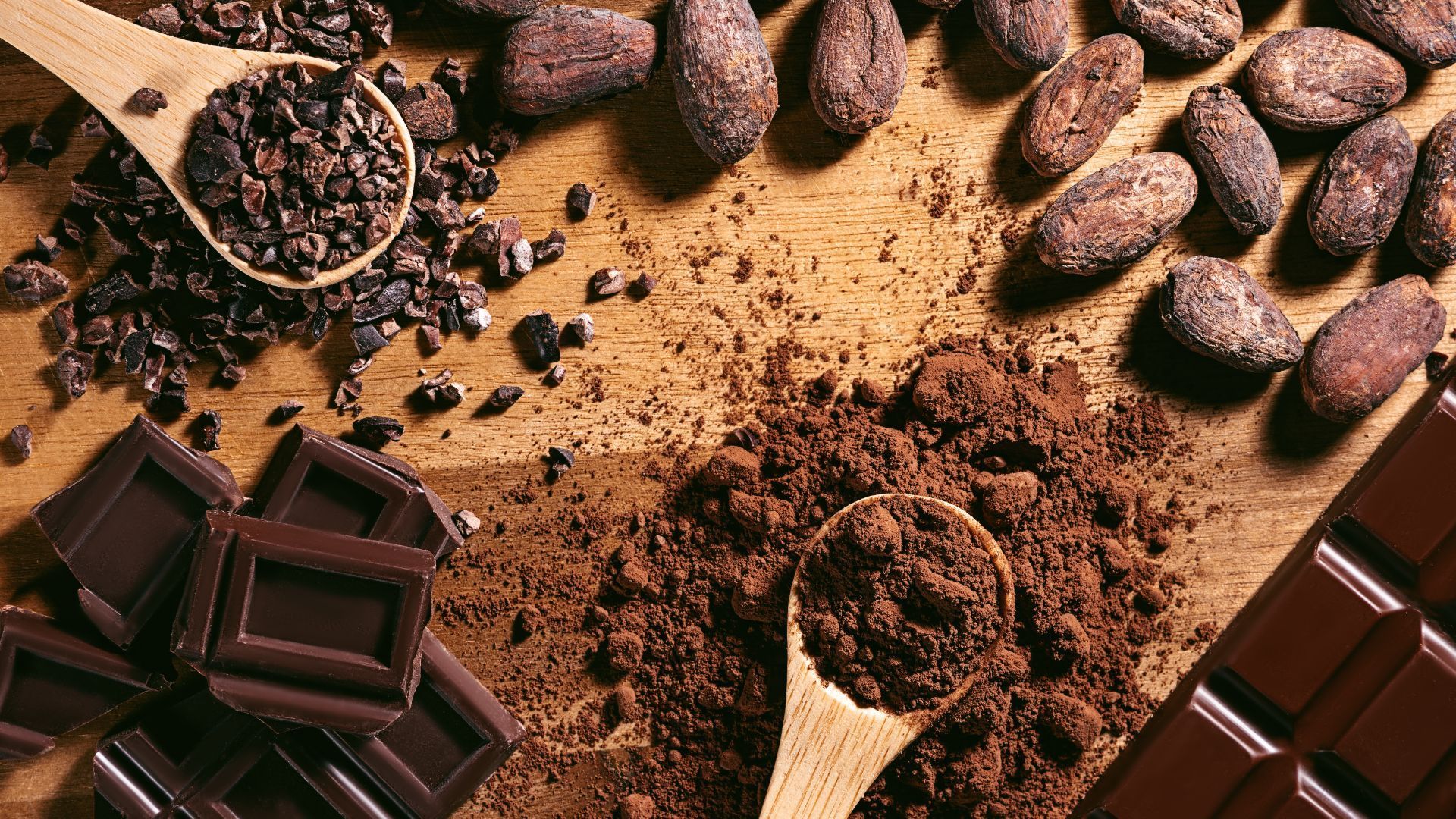 A wooden table topped with chocolate , cocoa beans , and cocoa powder.