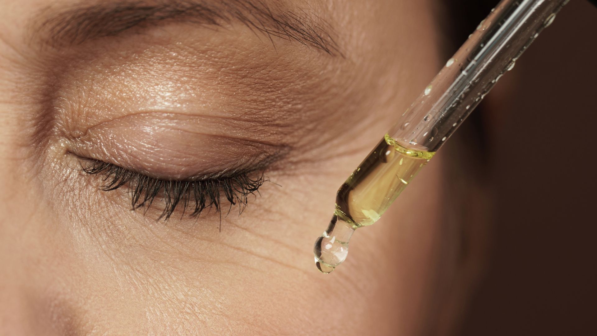 A woman is applying a drop of oil to her eye.