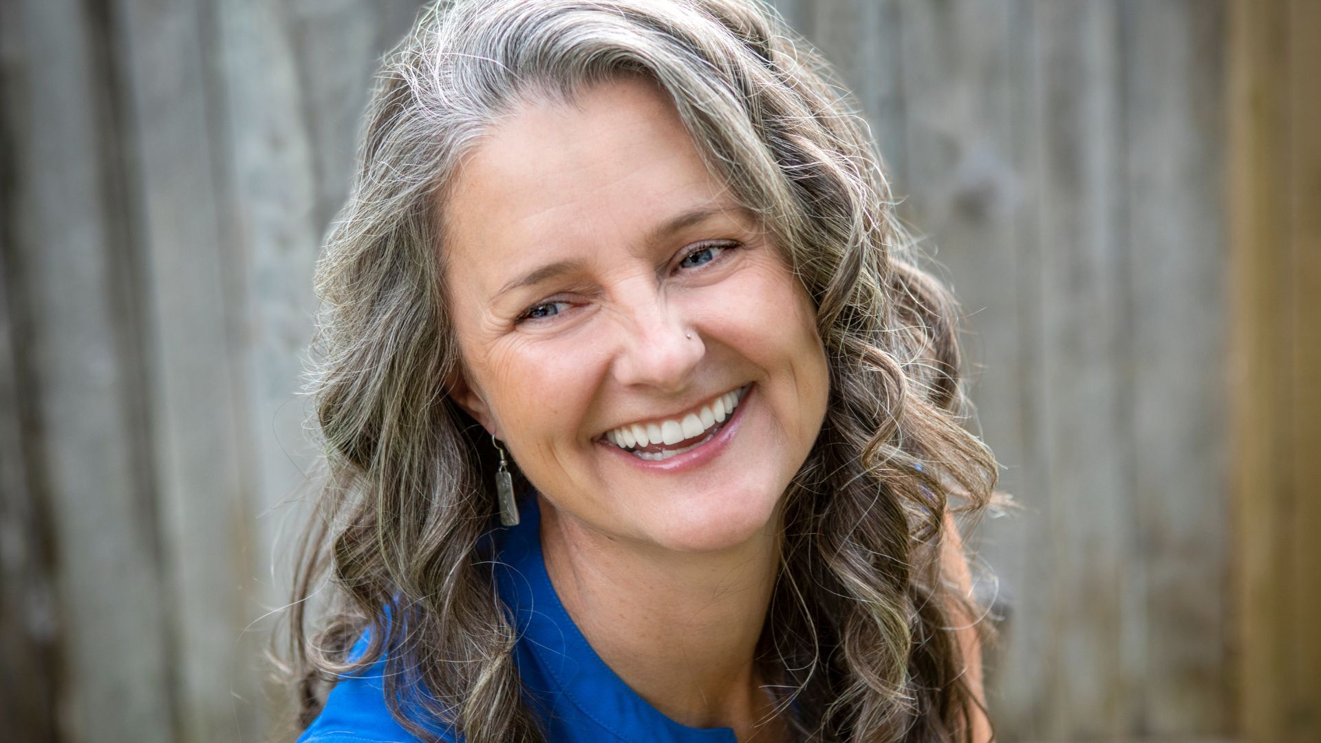 A woman with gray hair is smiling and wearing a blue shirt.