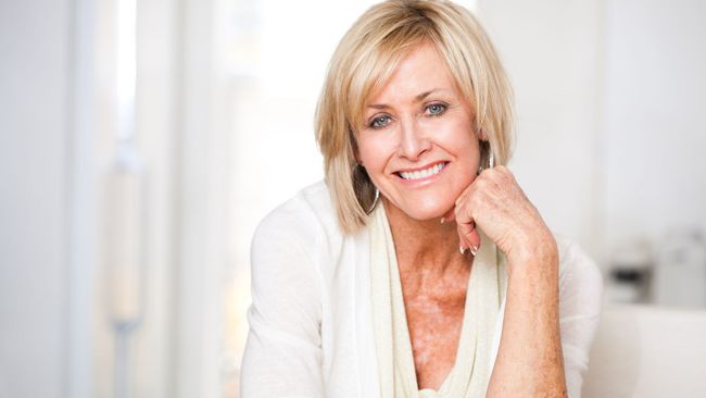 A woman in a white shirt is smiling with her hand on her chin.