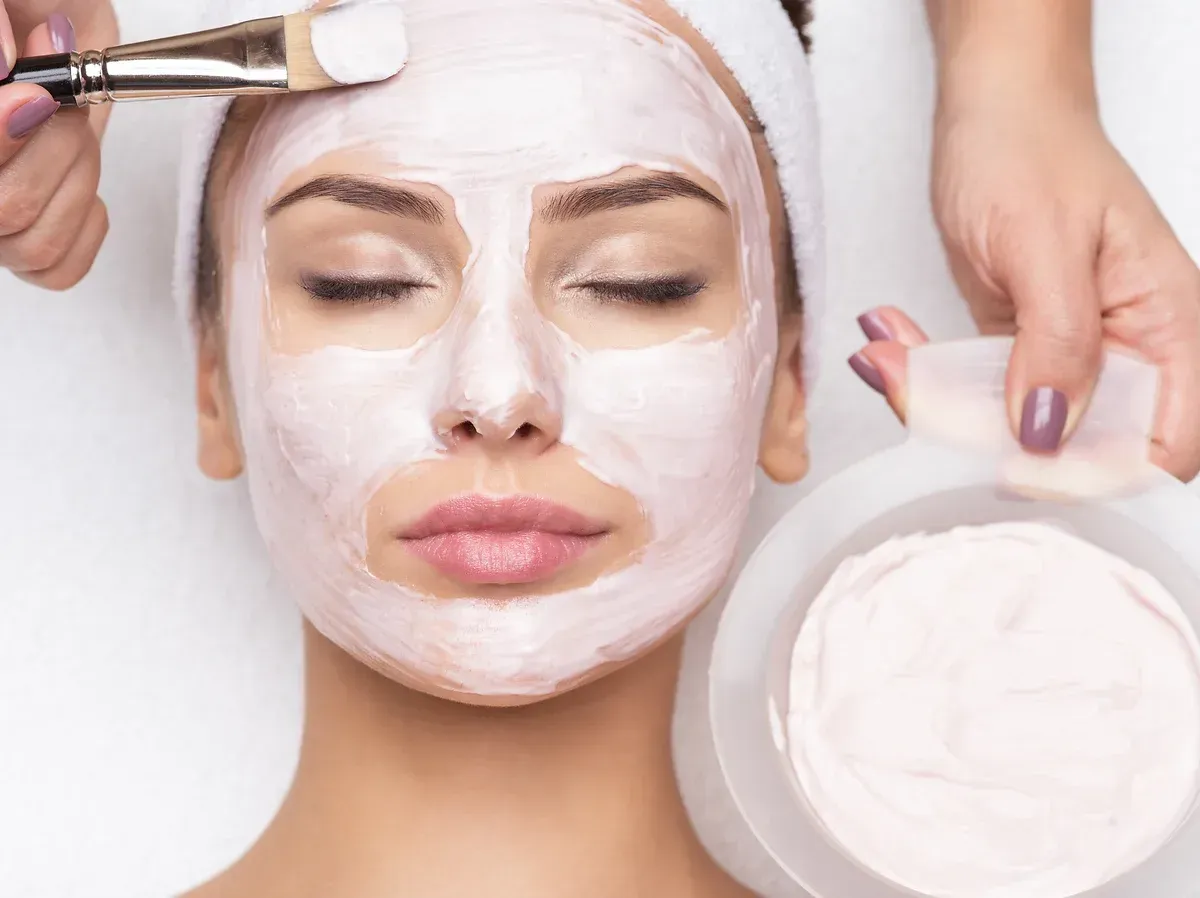 A woman is getting a pink facial mask at a spa.