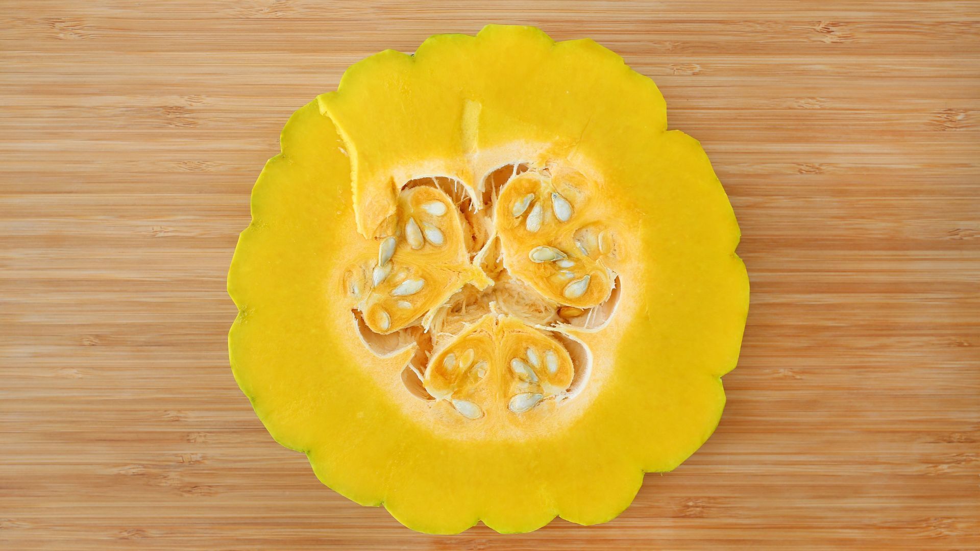 A yellow pumpkin is cut in half on a wooden cutting board.