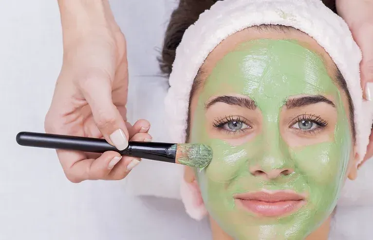 A woman is getting a green mask on her face.