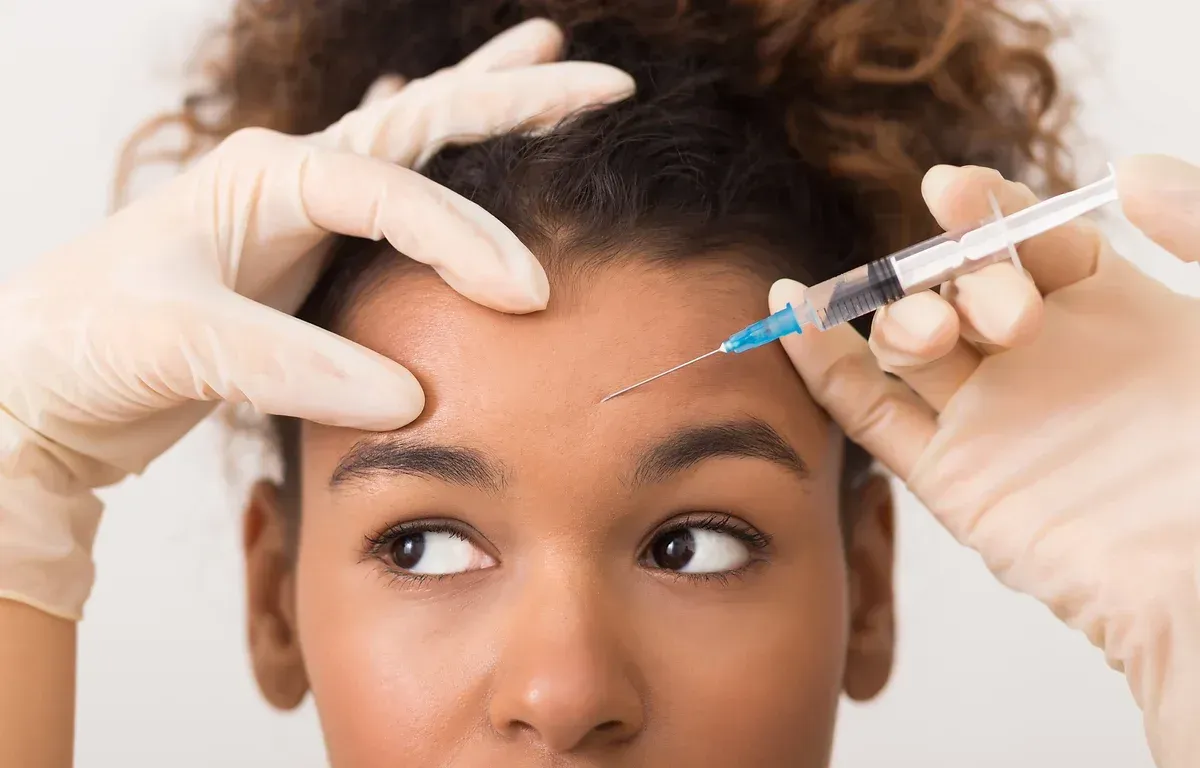 A woman is getting a botox injection on her forehead.