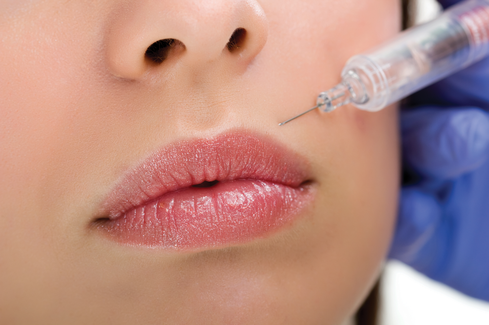 A woman is getting a botox injection in her lips.
