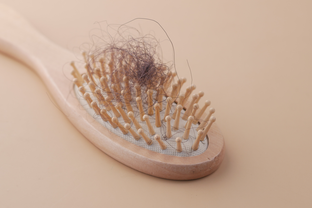 A wooden hairbrush with a bunch of hair on it.