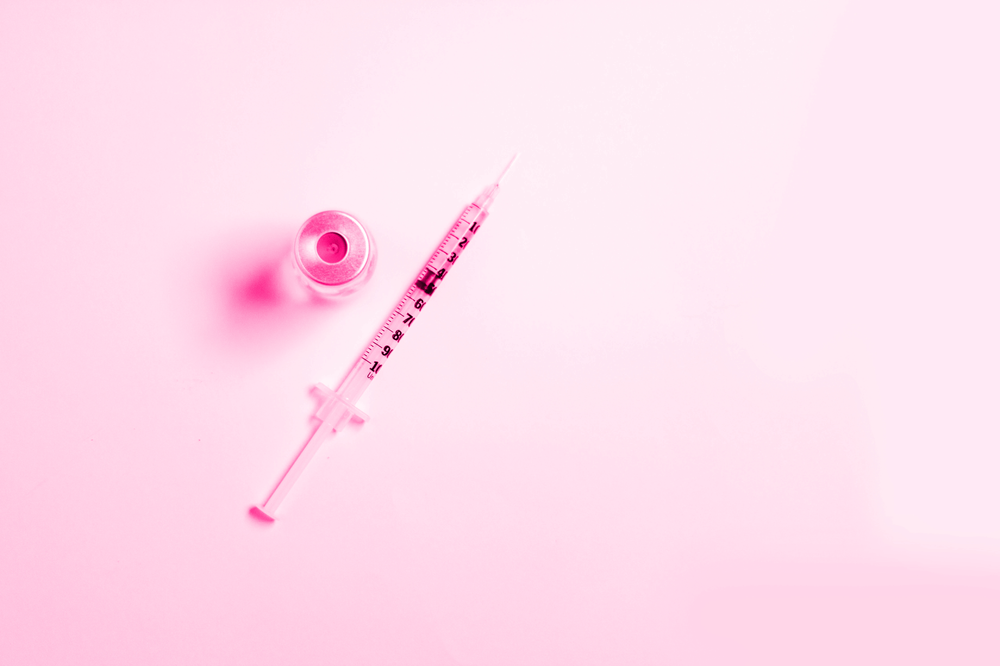 A syringe and a bottle of liquid on a pink background.