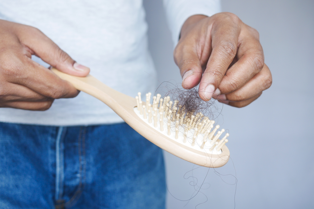 A man is holding a wooden brush with hair falling out of it.