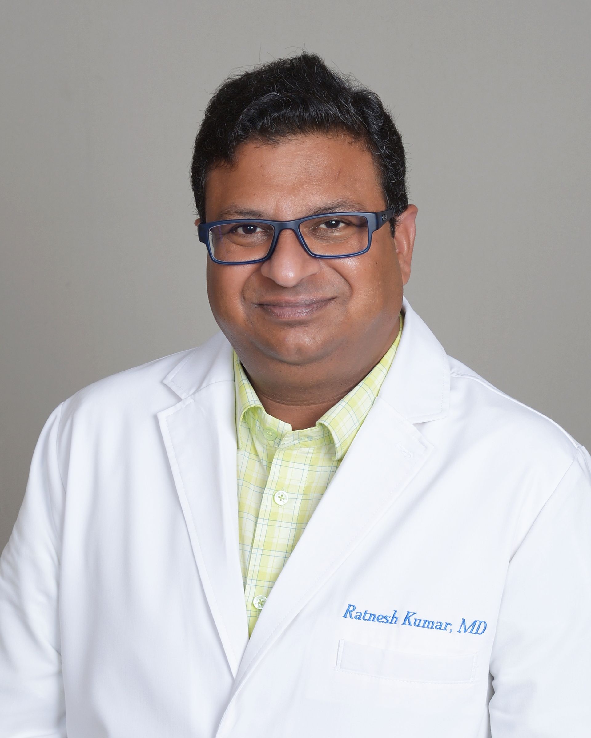 Man in white lab coat, wearing glasses, smiling; likely a doctor.