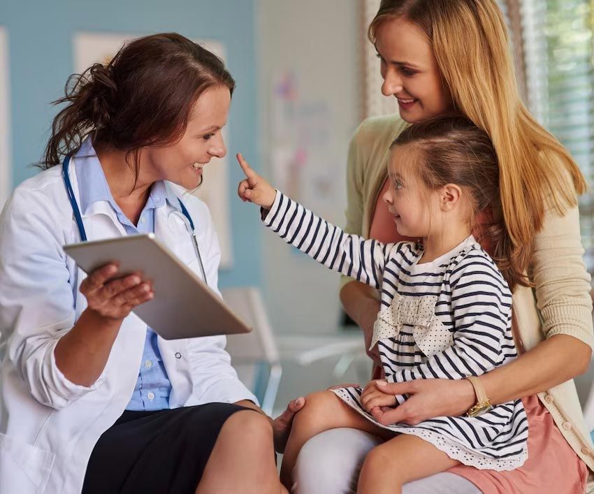 Doctor examining a young girl pointing at her nose while the mother watches.
