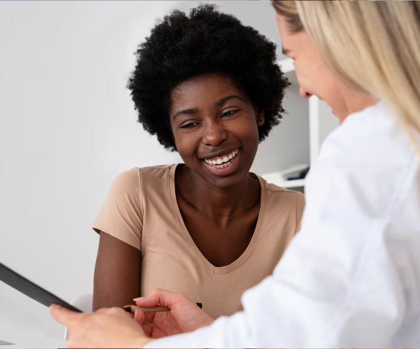 Black woman smiles while reviewing documents with a doctor in a white coat in a medical office.