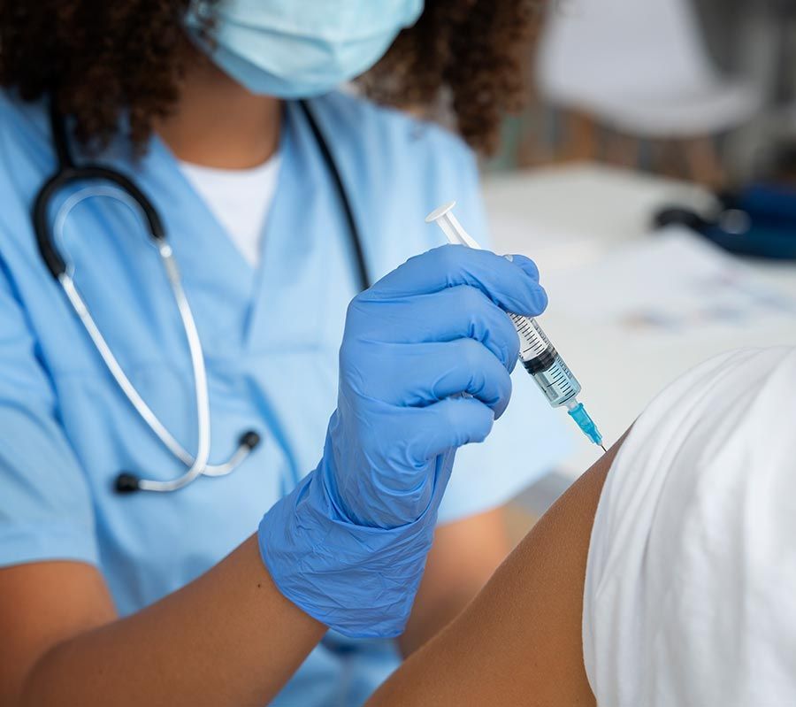 Nurse in blue scrubs gives a shot in the arm with a syringe.