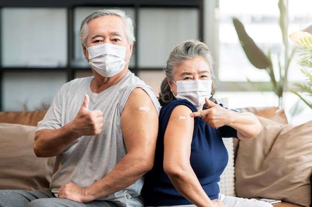 Elderly couple wearing masks, showing vaccine bandages, giving thumbs up and arm flex.