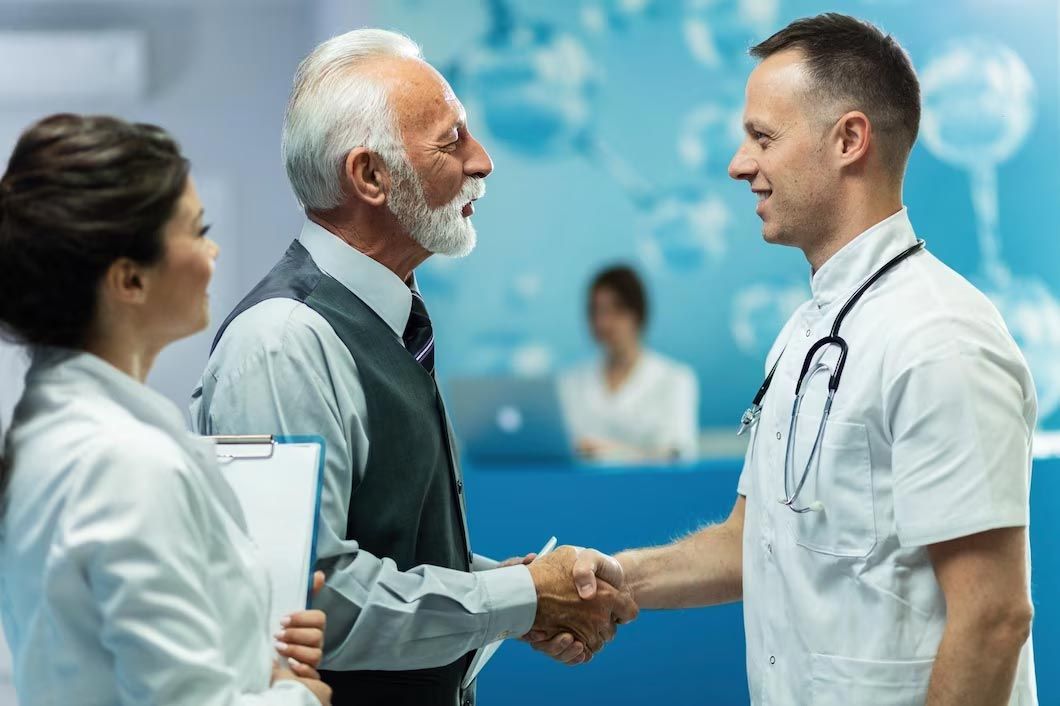 Doctor shaking hands with patient, another medical professional observes in a clinical setting.
