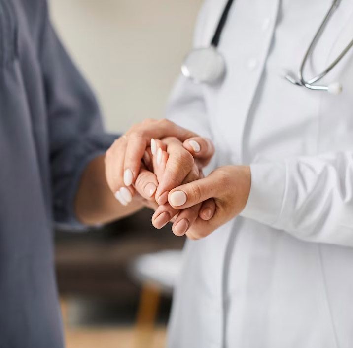 Doctor holding patient's hand; empathy and support. Doctor in white coat, stethoscope; hands close up.