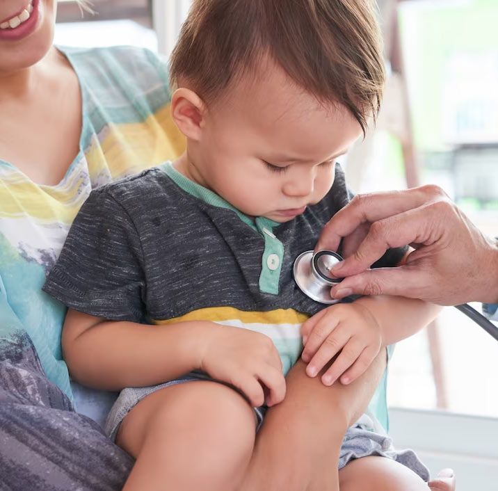 Baby sitting on mother's lap getting checked by doctor with a stethoscope.