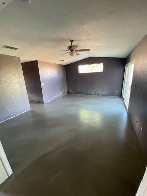 A large empty room with a ceiling fan and a window.