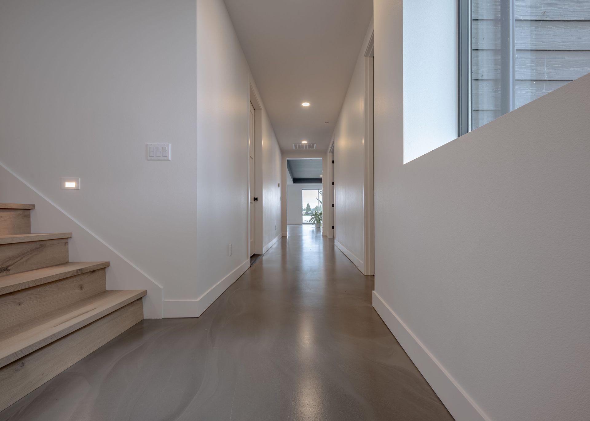 A long hallway with stairs and a window in a house.