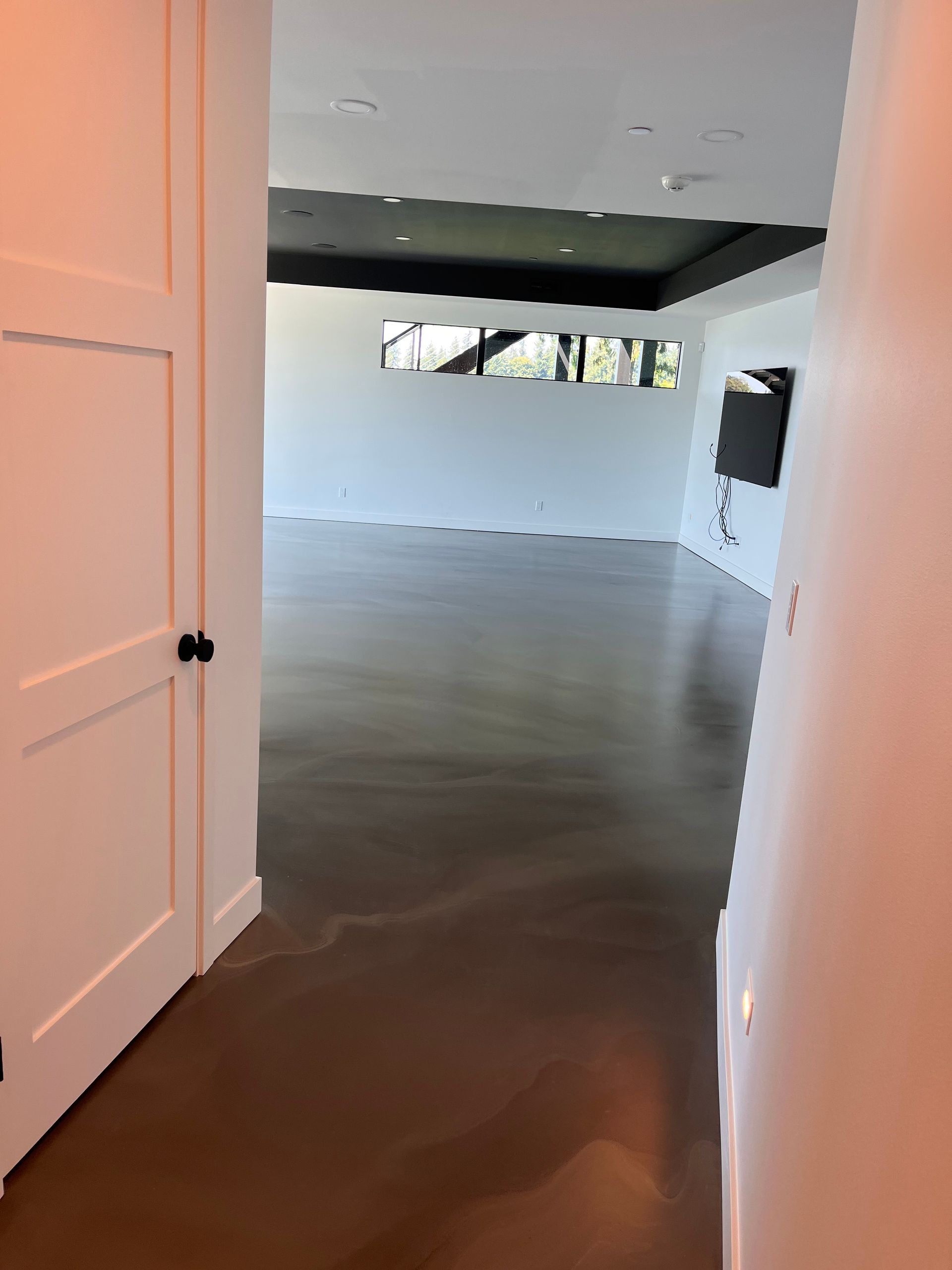 A hallway leading to a large empty room with hardwood floors and white walls.