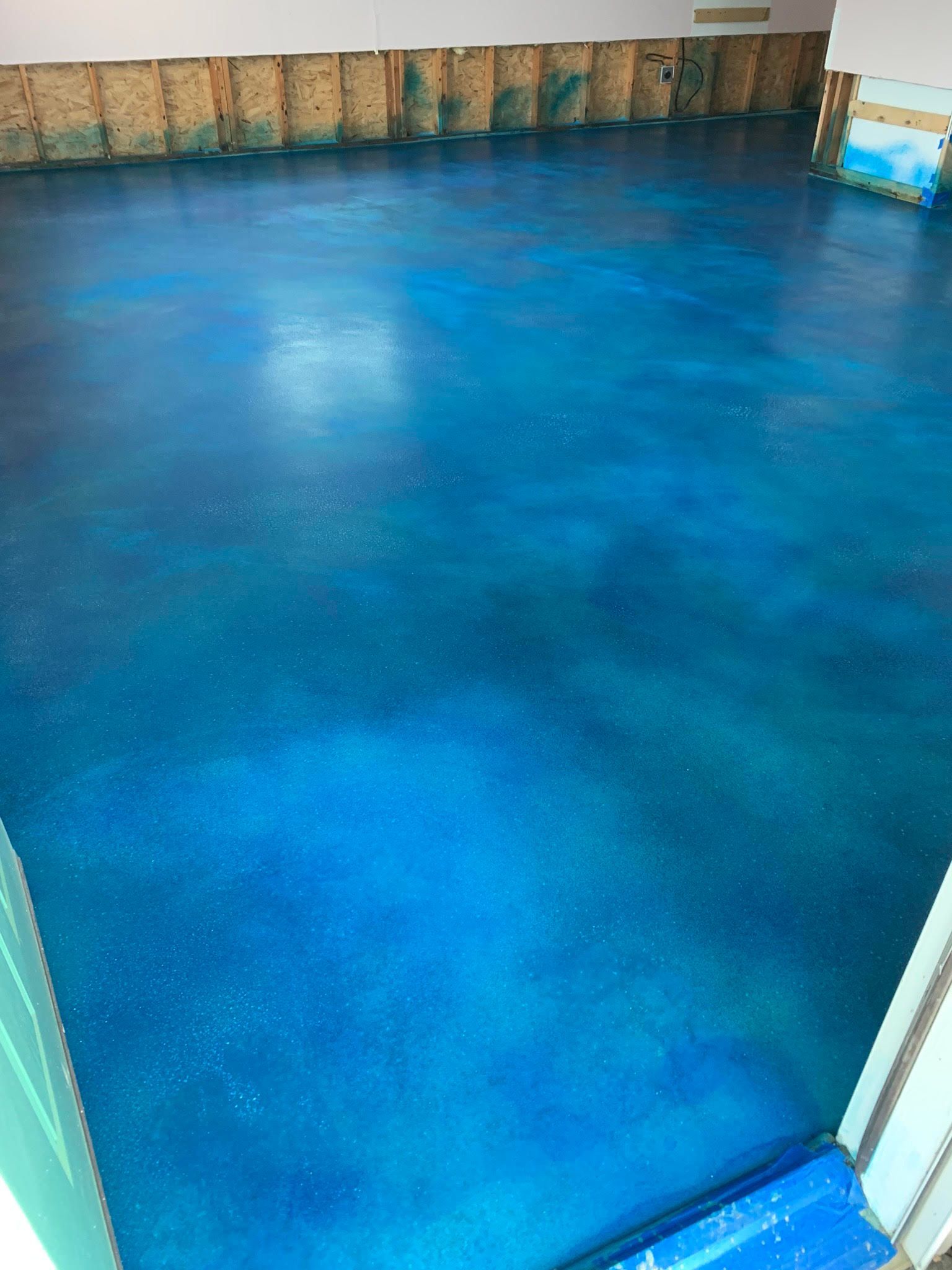 A blue concrete floor in a room with a white wall.