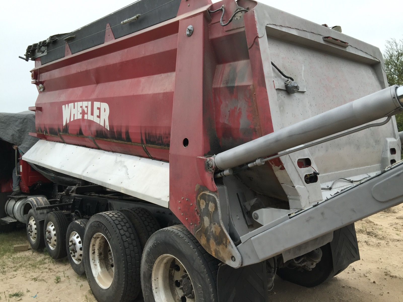 A red and white dump truck is parked in a dirt field.