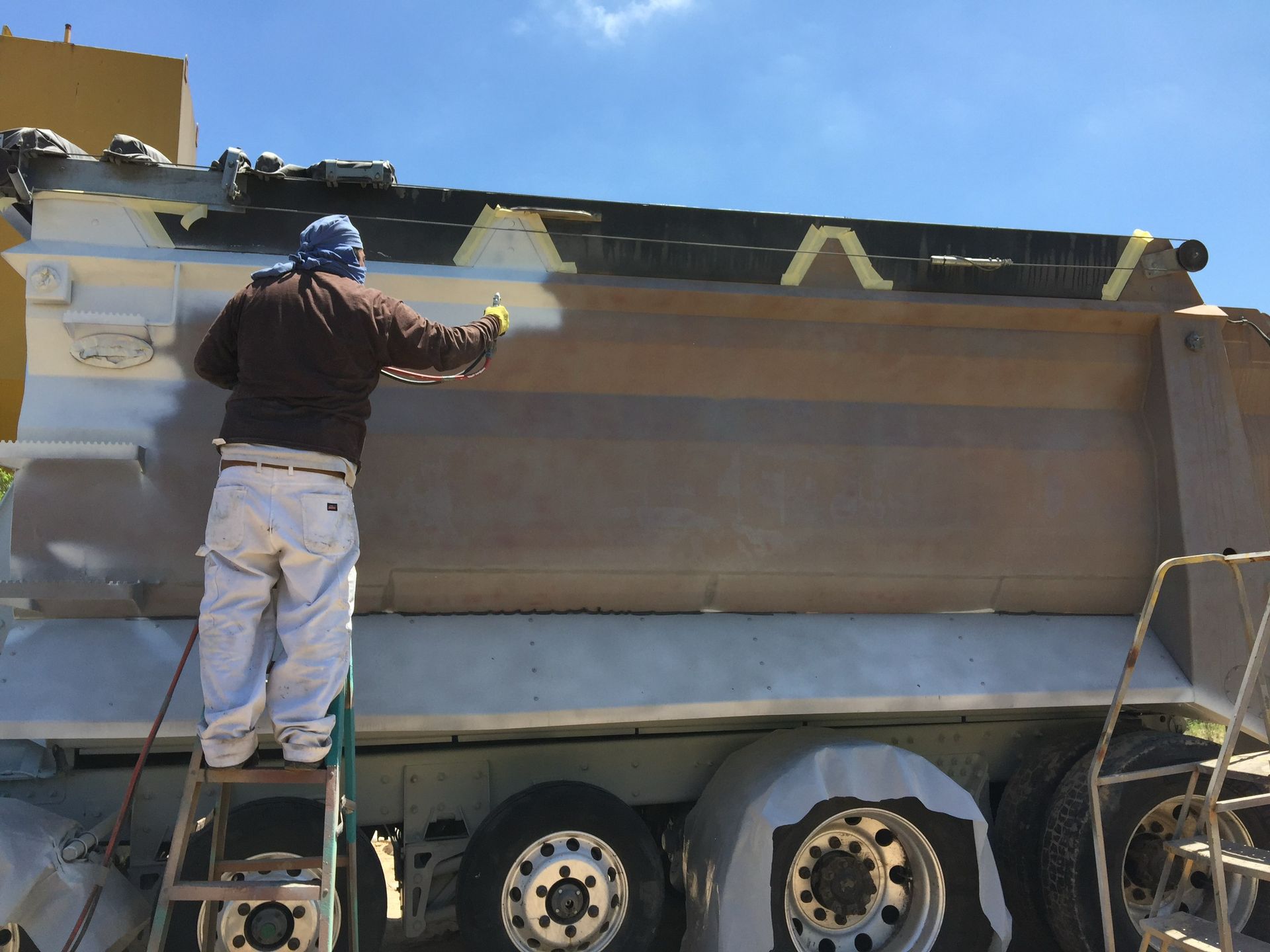 A man is painting the side of a dump truck