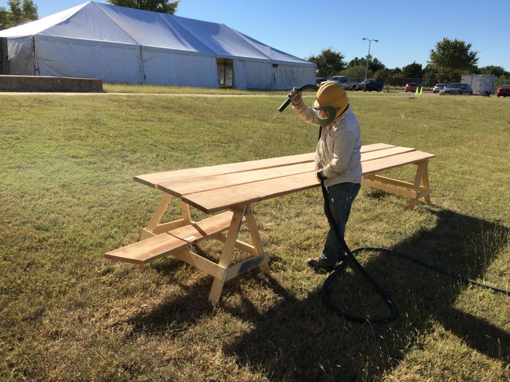 A man is standing next to a wooden picnic table in a field.