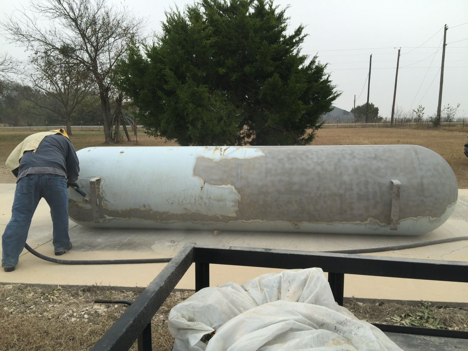A man is sandblasting a large propane tank