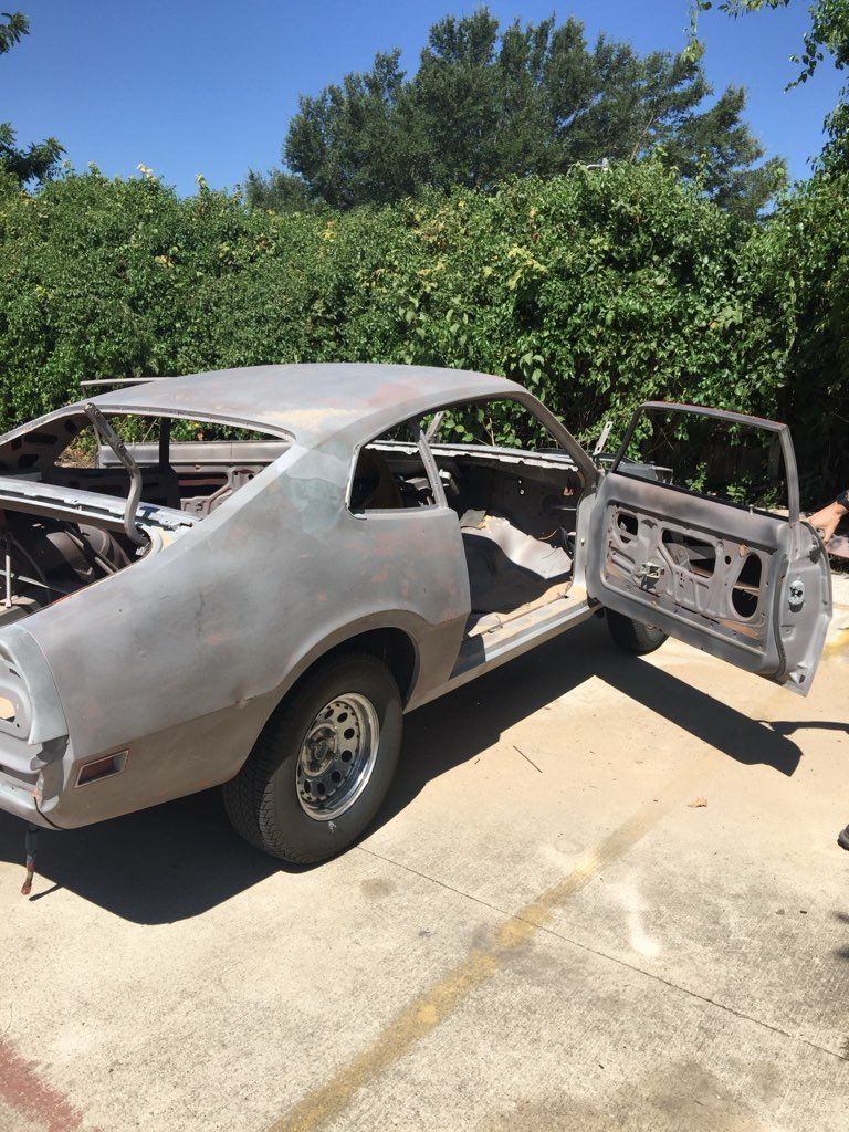 A gray car is parked in a parking lot with its doors open.