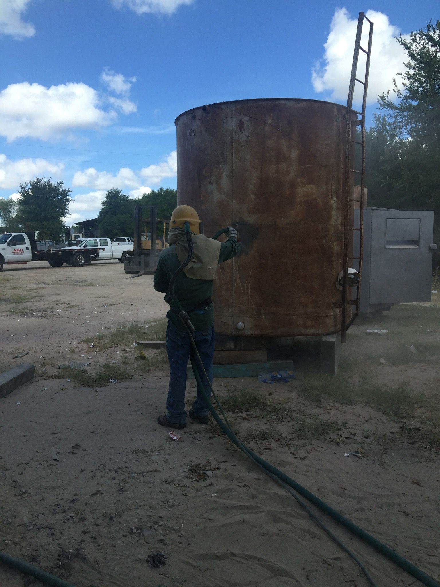 A man is sandblasting a large rusty tank