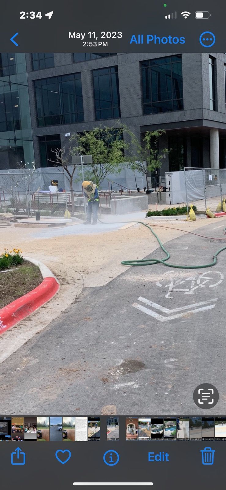 A phone screen shows a construction site with a hose spraying water on the ground.