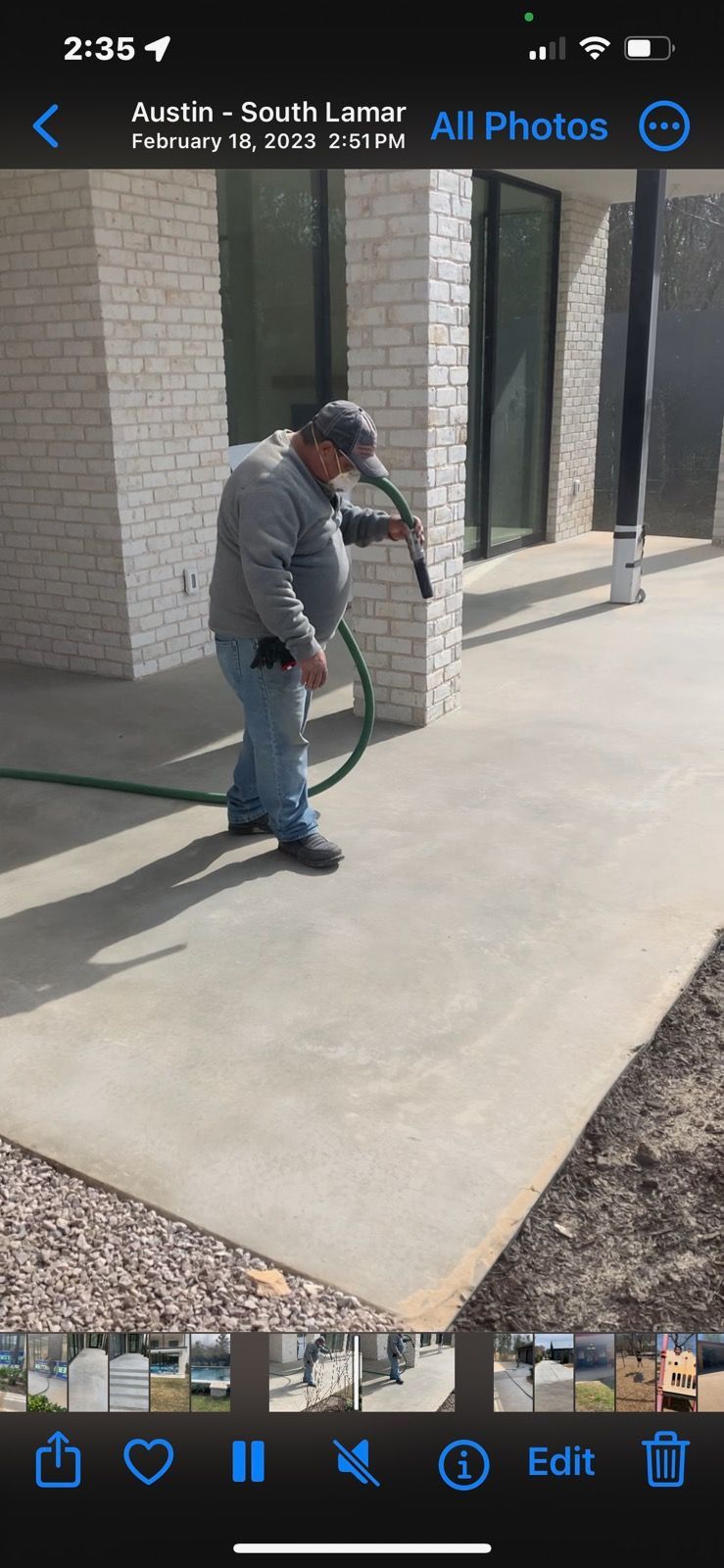A man is watering a concrete sidewalk with a hose.