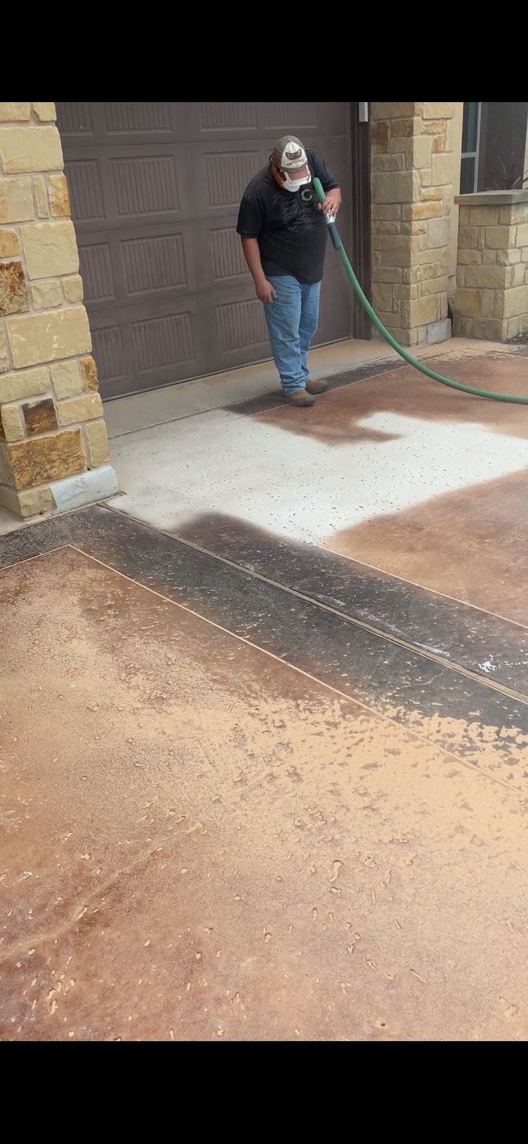 A man is watering a concrete driveway with a hose.