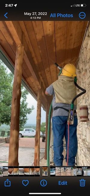 A man wearing a yellow hard hat is sanding the ceiling of a building.