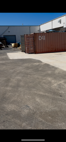 Exterior of an industrial area with shipping containers on a concrete lot and a blue sky.