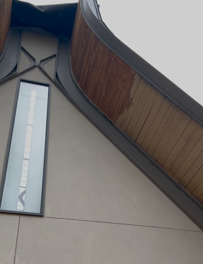 Exterior of building with wooden awning, vertical window, and gray walls.