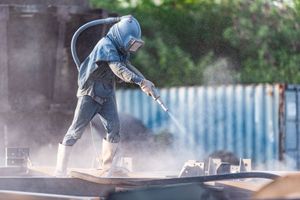 A man is sandblasting a piece of metal.