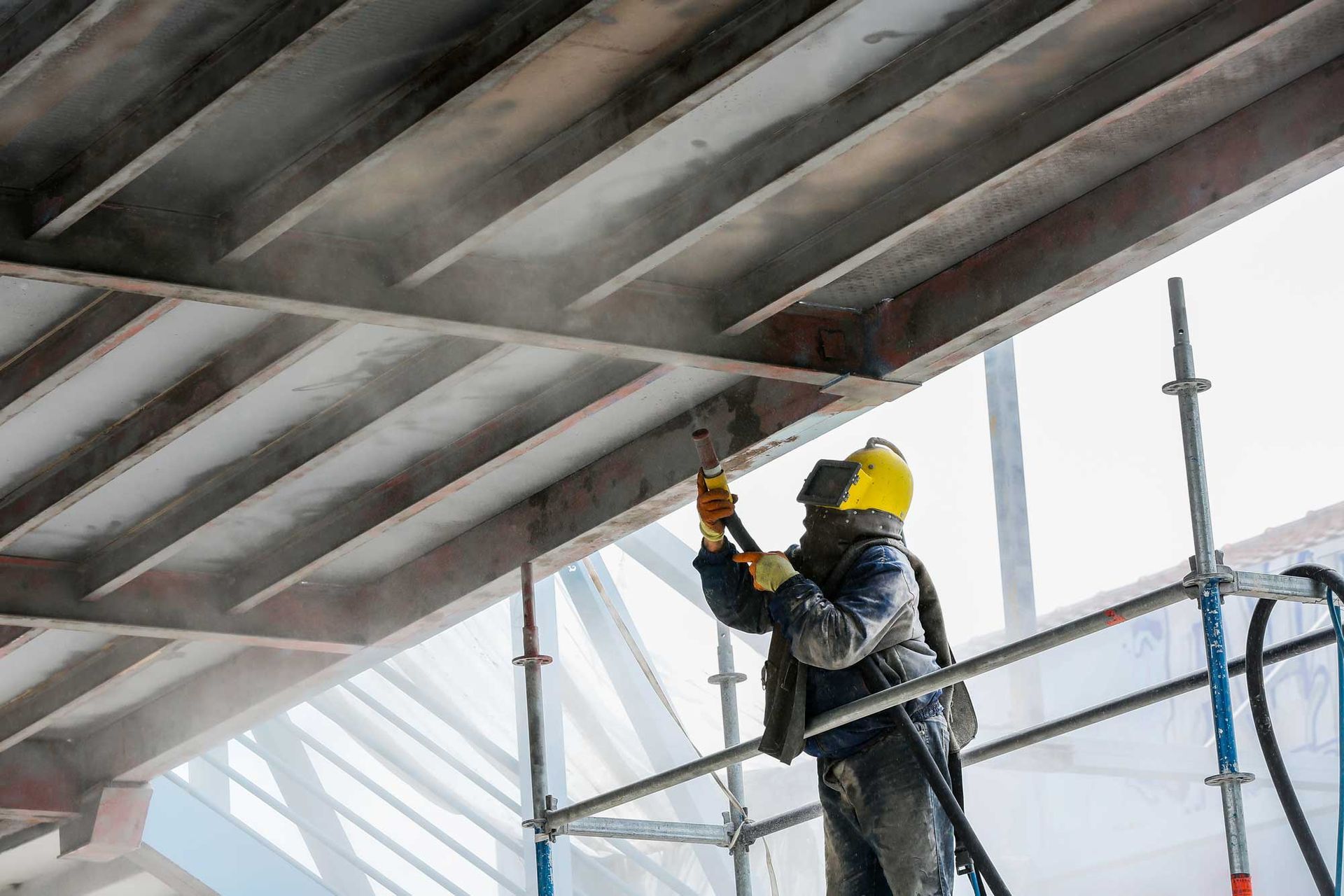 A man is standing on a scaffolding painting a bridge.