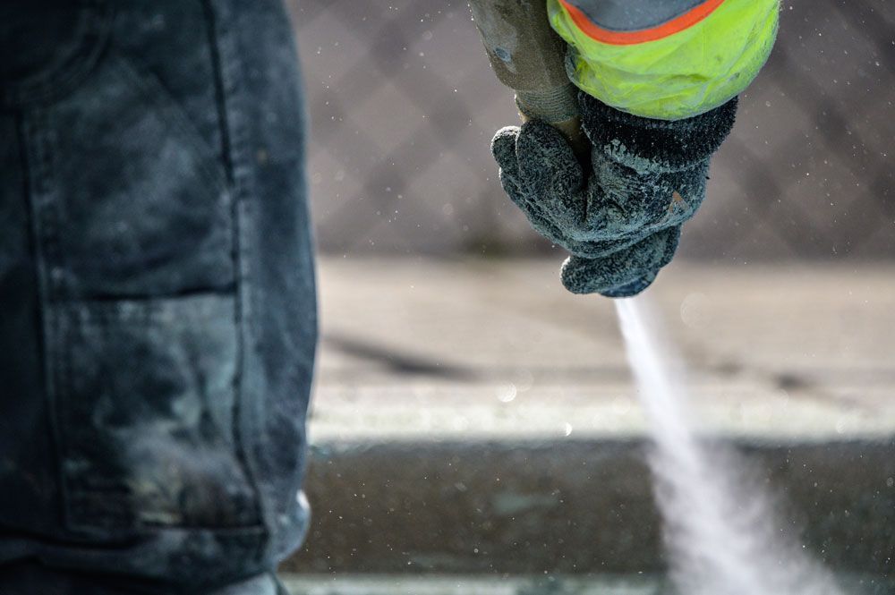 A person is using a high pressure washer to clean a concrete surface.