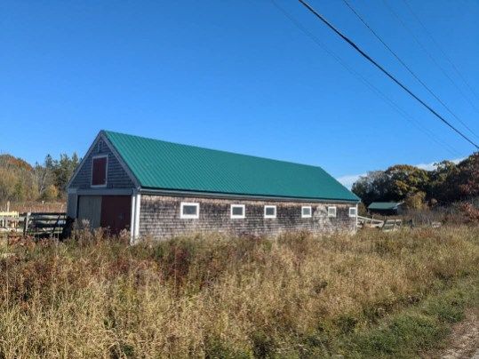 Gray barn with green roof and small windows, in a field on a sunny day.