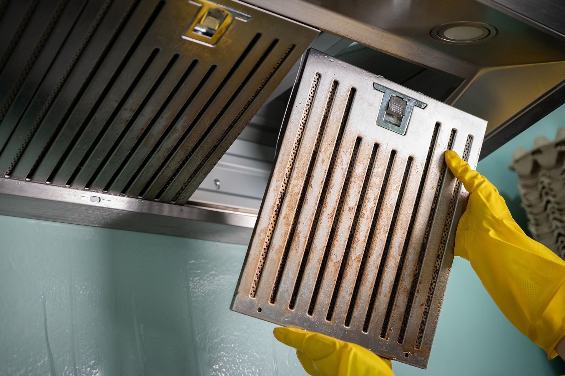 A person wearing yellow gloves is holding a dirty exhaust fan filter.