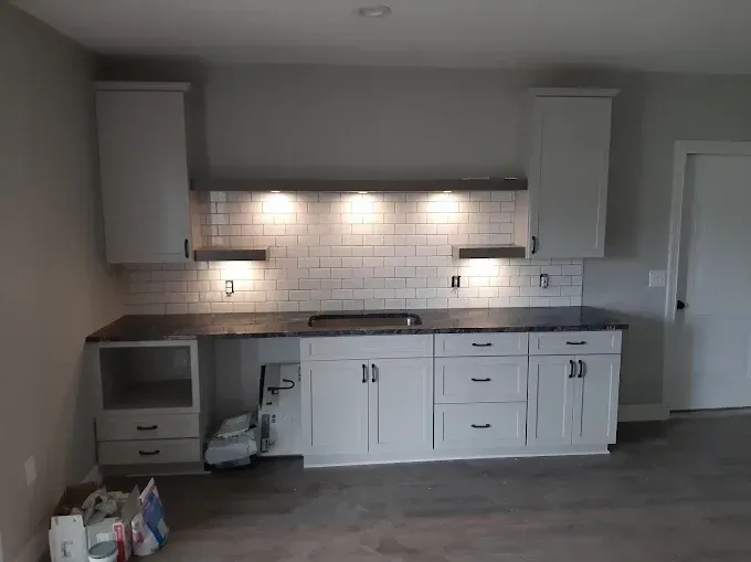 Gray and white kitchen cabinets with black countertops, a backsplash, and under-cabinet lighting.