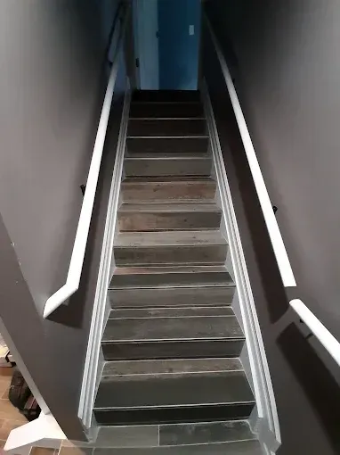Staircase with dark grey steps, white handrails, and grey walls.